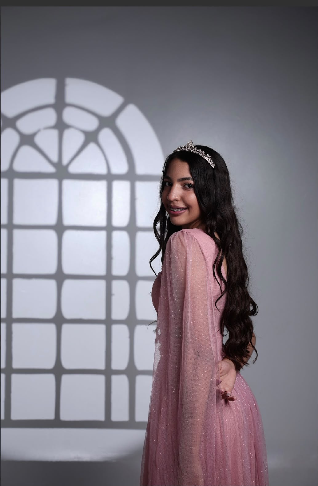 Ana Laura com vestido rosa e tiara, sorrindo sobre o ombro